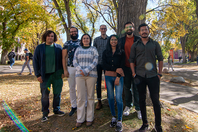 A group of six students and their professor standing in front of green plants.