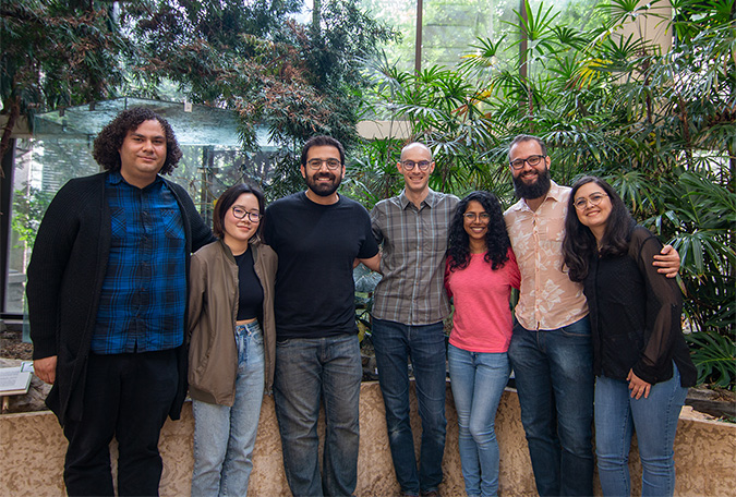 A group of six students and their professor standing in front of green plants.
